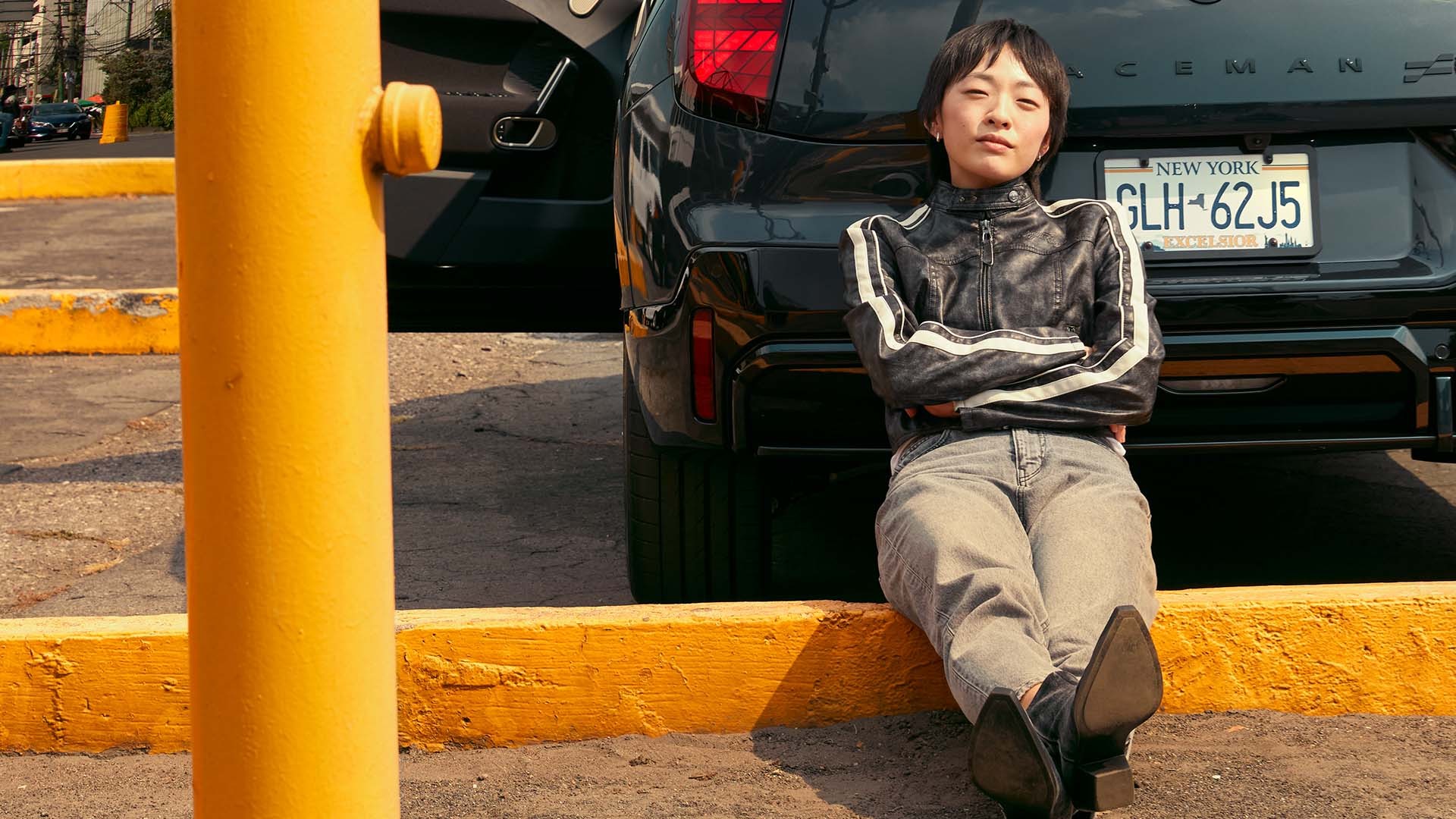 Person sitting on the ground leaning against the rear of a black MINI vehicle